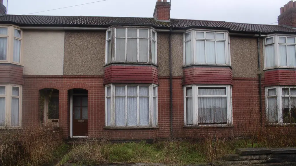 Empty 1950s terraced house with faded curtains and an overgrown garden