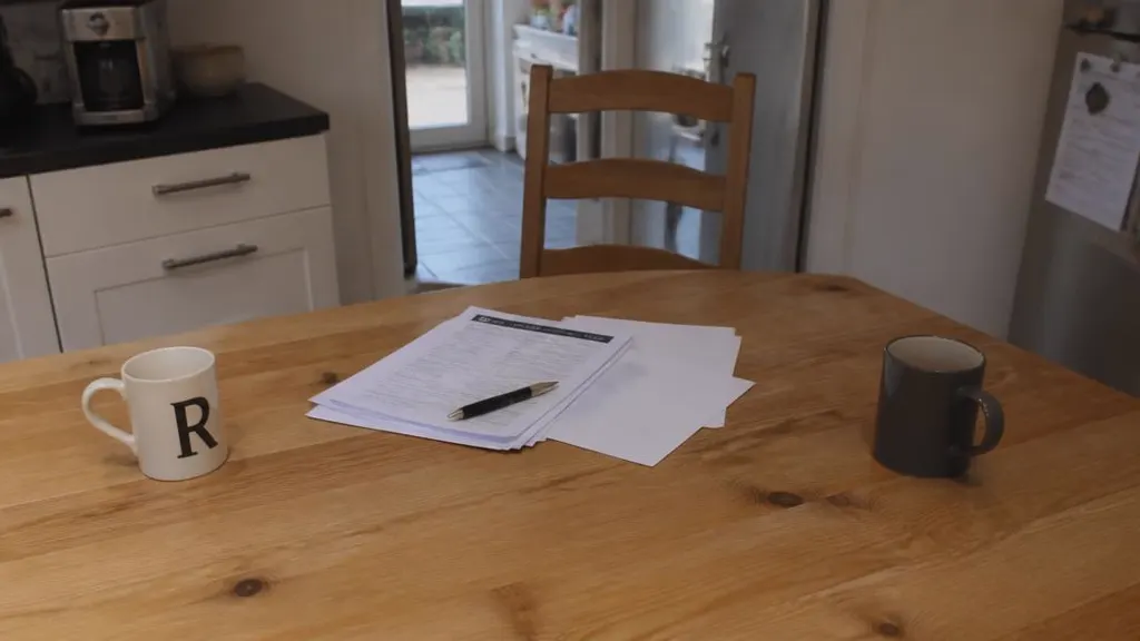 Two mugs at opposite ends of a kitchen table with paperwork between them