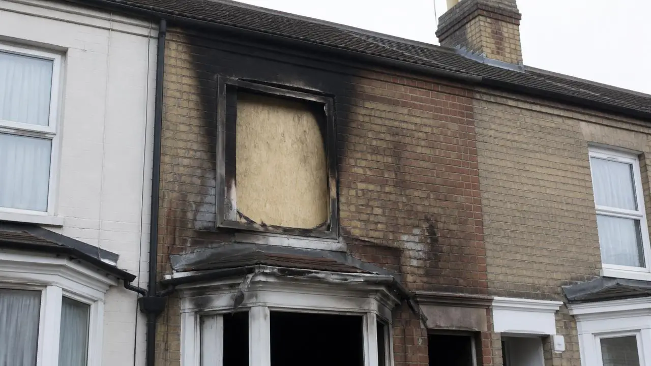 Fire damaged house exterior with soot marks and a boarded window