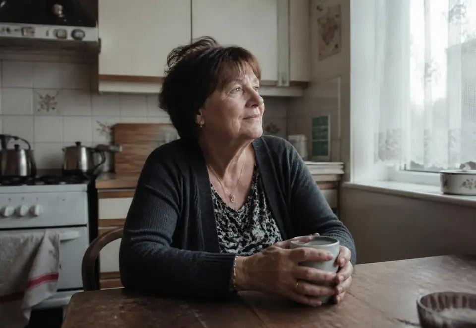A woman in her 60s at a kitchen table, quiet relief