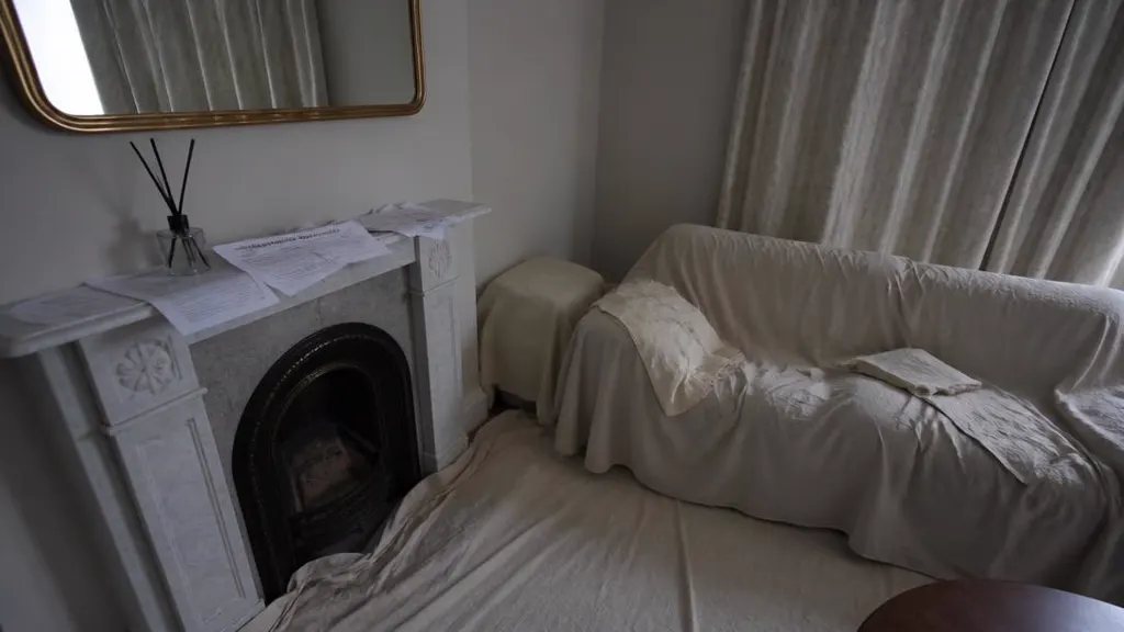 Unoccupied living room with dust sheets over the sofa and papers on the mantelpiece